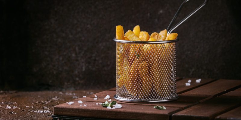 Traditional french fries potatoes served in frying basket with salt, thyme on wooden board over brown texture background. Homemade fast food